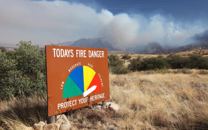 Un feu de forêt brûle à l'arrière-plan d'un panneau de danger d'incendie dans les montagnes Organ du Nouveau-Mexique. (DenisTangneyJr./ Getty Images Signature)