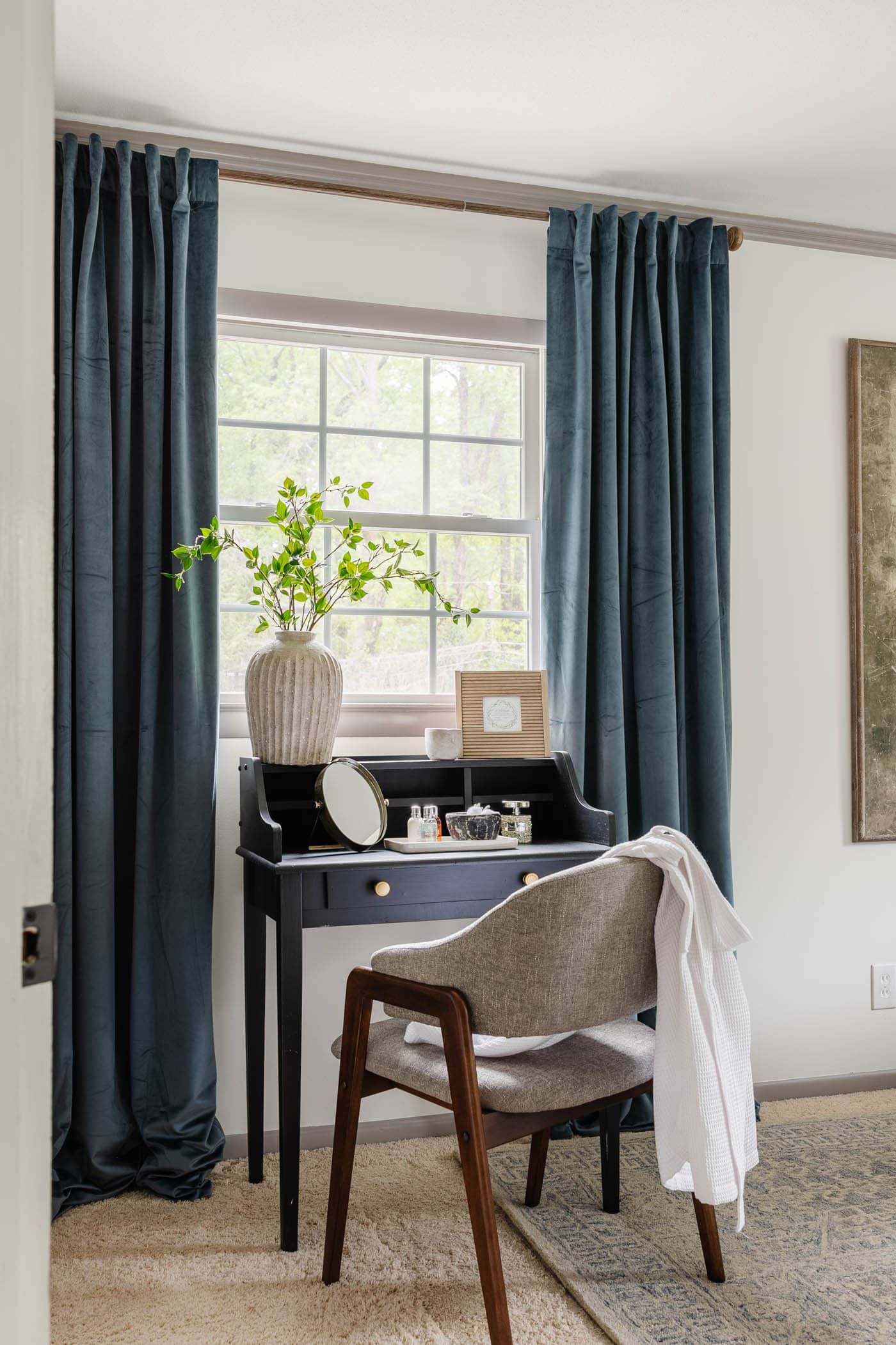 vanité de chambre à coucher devant une fenêtre avec des rideaux bleus et un vase de tiges