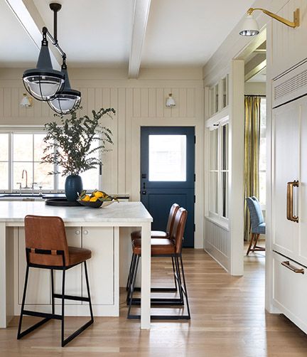 Tabourets de comptoir en cuir dans une magnifique cuisine blanche avec des fenêtres intérieures-design de Brian Paquette dans AT HOME (Gibbs Smith, 2021). # kitchendesign #counterstools #coastalstyle