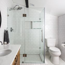 La douche met en valeur les carreaux de métro surdimensionnés de 5 pouces sur 7 qui tapissent ses murs, ainsi que ceux de l'alcôve de la baignoire; la pose du carreau dans un motif à chevrons avec du coulis gris renforce son intérêt visuel. 